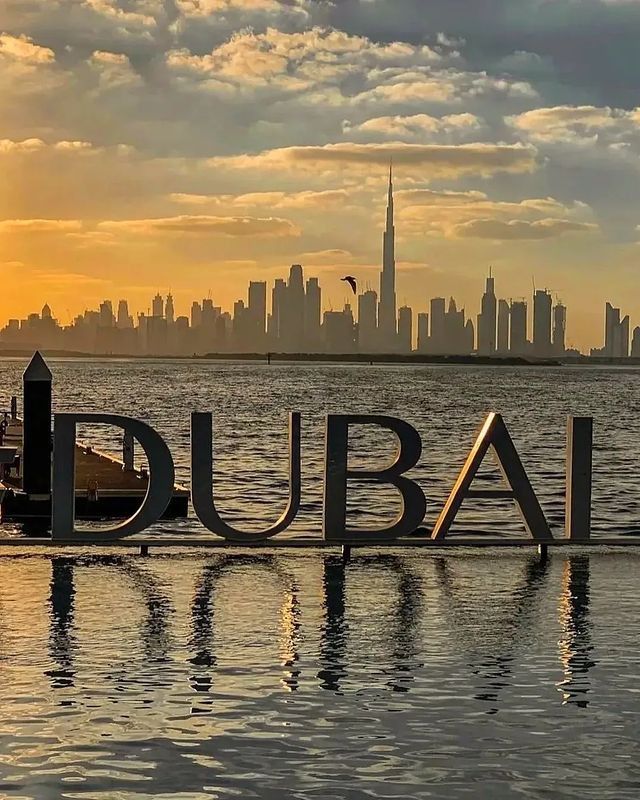 the word dubai is in front of a large body of water with a cityscape in the background