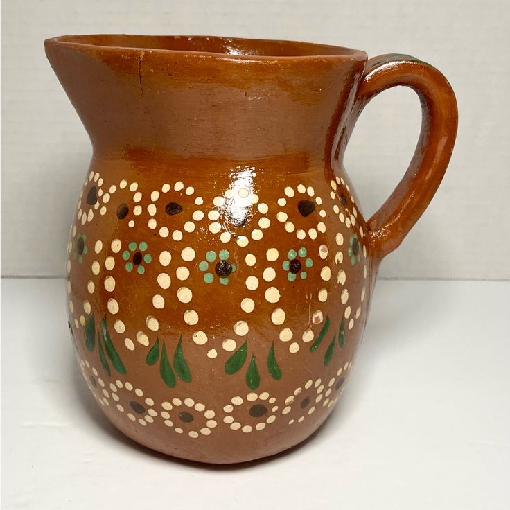 a brown vase with white and green designs on it's sides, sitting on a table