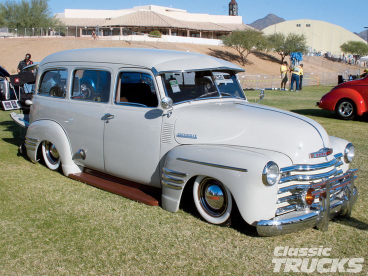 an old car parked on top of a grass covered field next to other cars and people