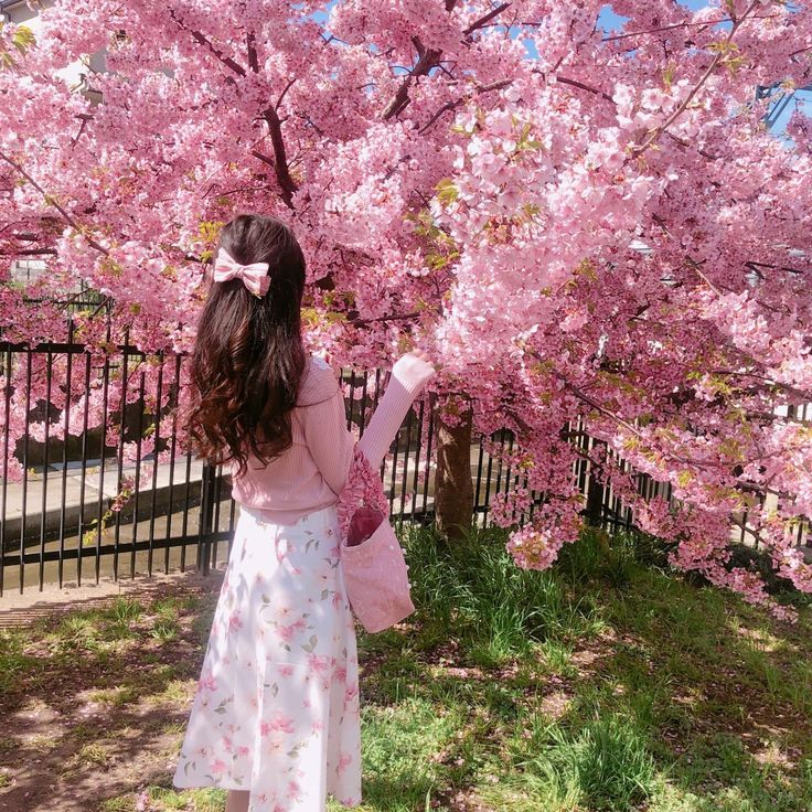 a girl in a pink dress standing under a tree with pink flowers on it's branches