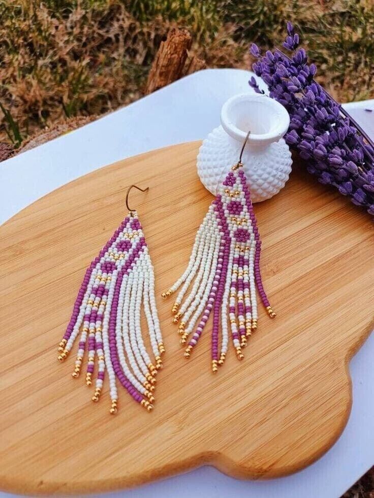 a pair of beaded earrings sitting on top of a wooden board next to lavender flowers