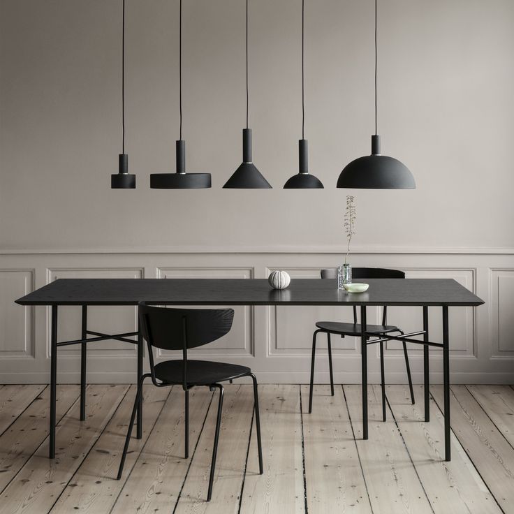 a dining table with black chairs and lights hanging from the ceiling in an empty room