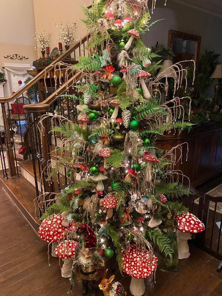 a christmas tree with ornaments on it in the middle of a room next to stairs