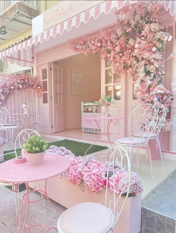 a pink and white house with flowers on the front porch, tables and chairs outside