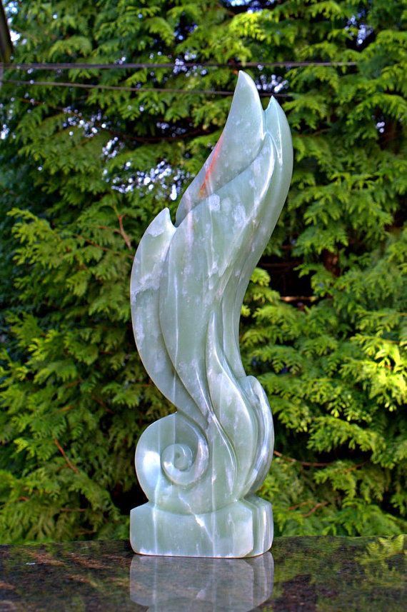 a white marble sculpture sitting on top of a table next to a green tree and bushes