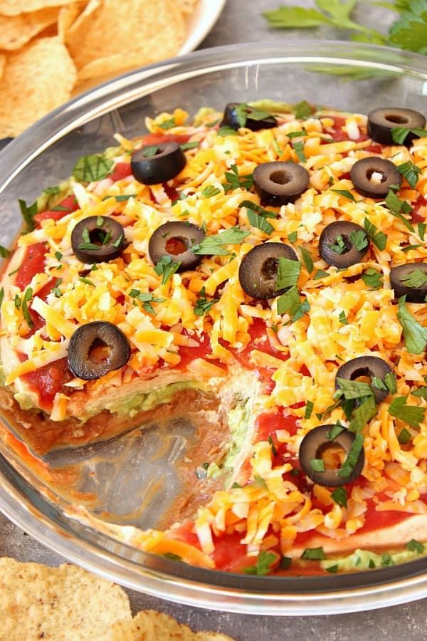 a pizza with olives, cheese and sauce in a glass dish next to chips