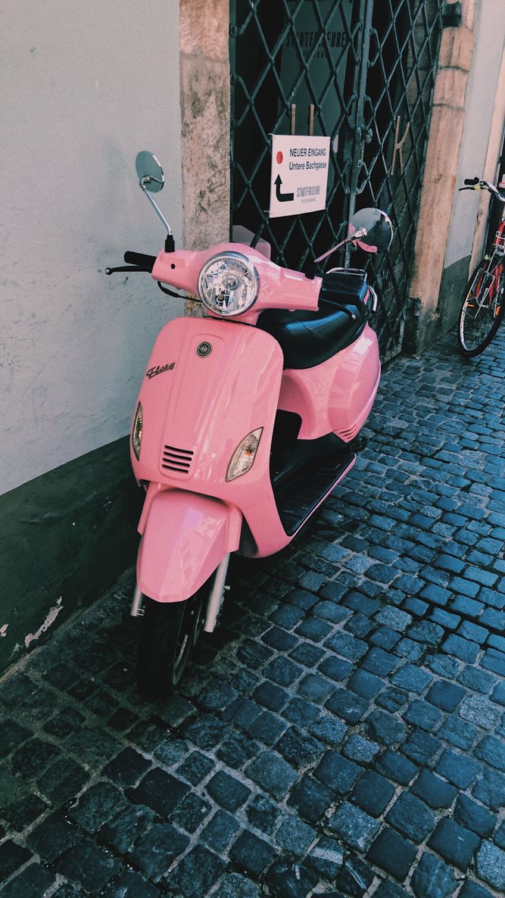 a pink scooter parked next to a building on a cobblestone street