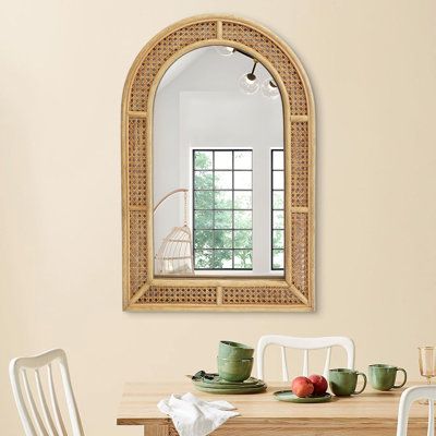 a dining room table with chairs and a mirror on the wall above it that has an arched window