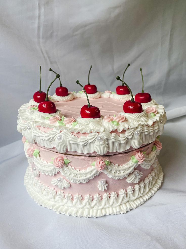 a three layer cake with cherries on top and pink icing, sitting on a white tablecloth