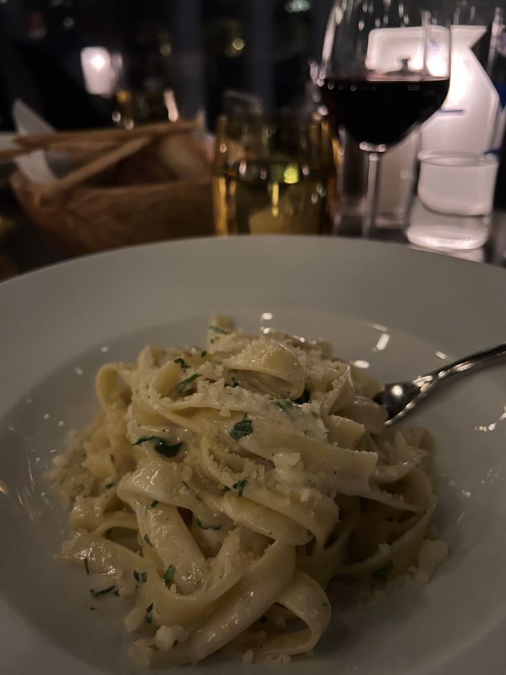 a white plate topped with pasta covered in sauce and parmesan cheese next to a glass of wine