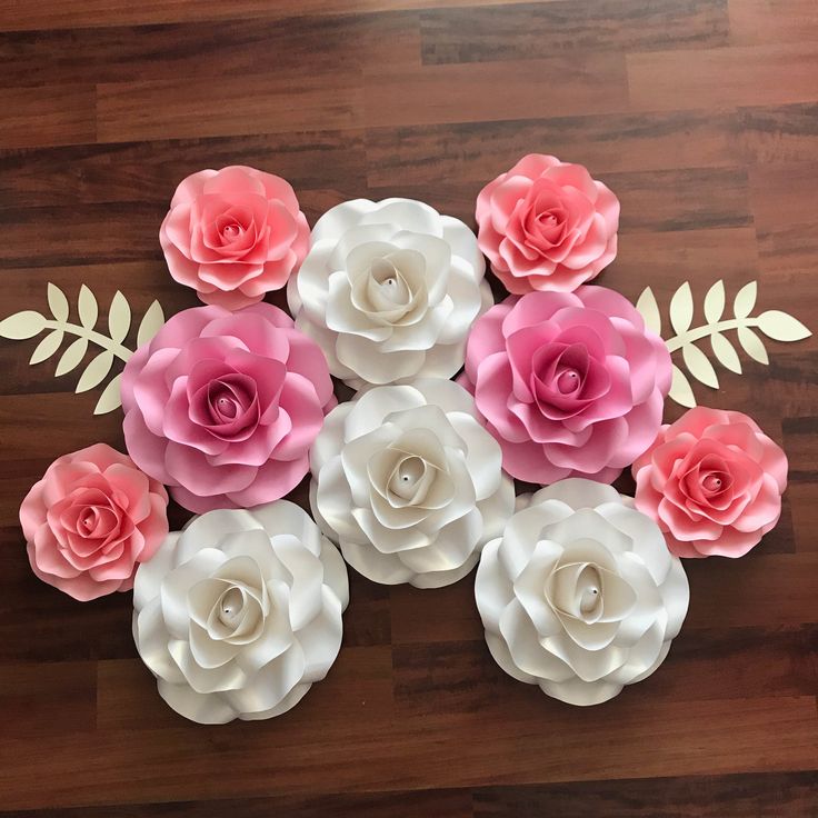 paper flowers are arranged on a wooden floor with leaves and stems in the center, as well as pink and white ones