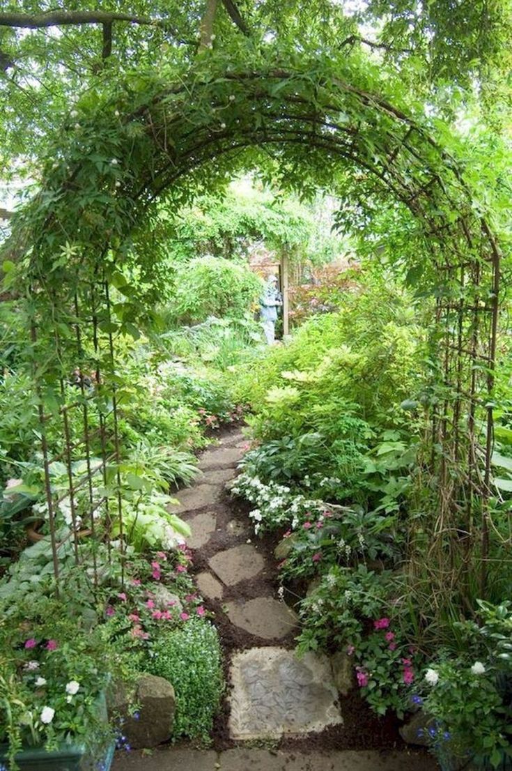 a garden with lots of plants and flowers on the side of it, including an arch