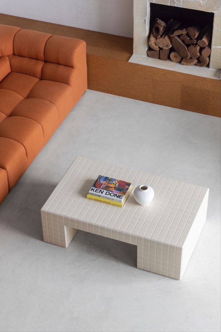 a living room with an orange couch and white coffee table in front of a fireplace