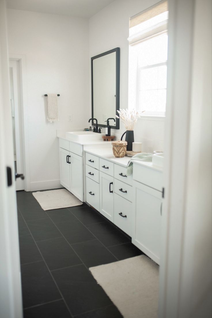 a white bathroom with black tile flooring and large mirror on the wall above it