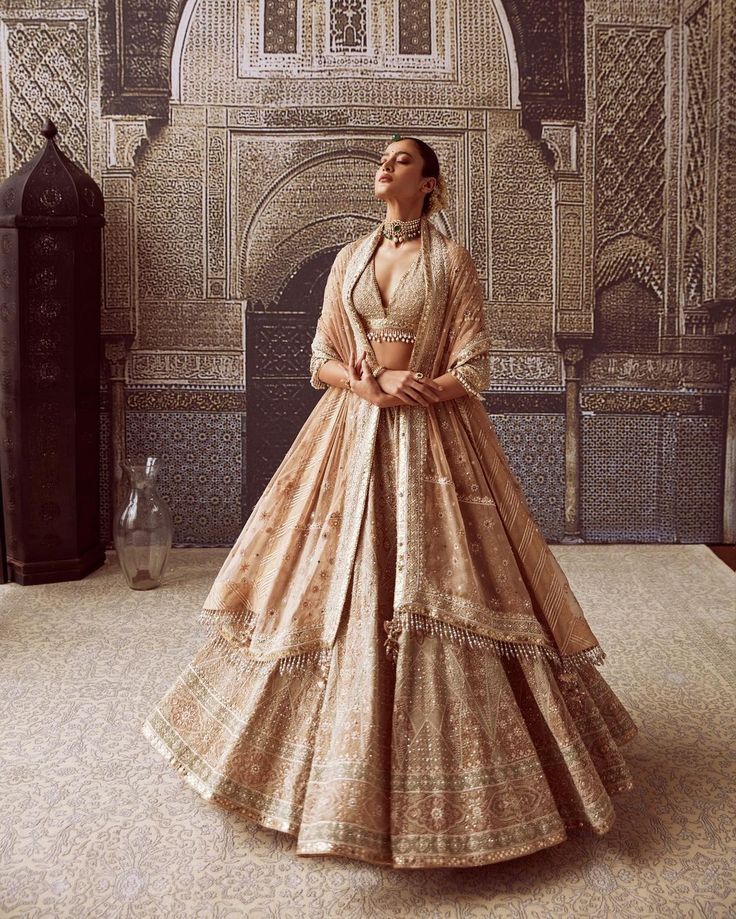 a woman standing in front of a wall with an intricate pattern on it and wearing a long dress