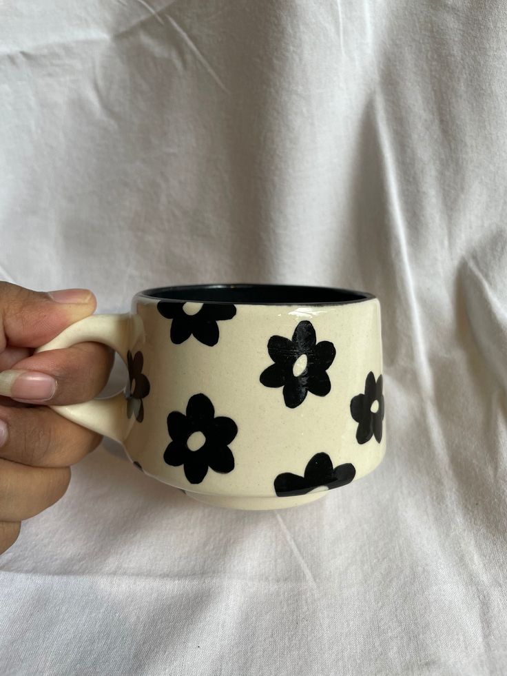 a hand holding a black and white flowered coffee cup on top of a white sheet