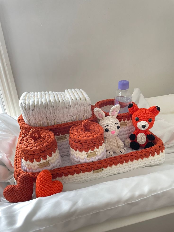 there is a crocheted tray with baby items on it and two stuffed animals