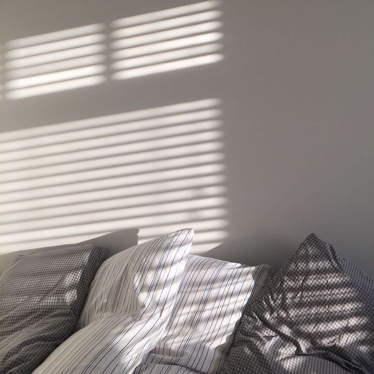 the sun is shining through the window blinds in this bedroom with bed linens and pillows