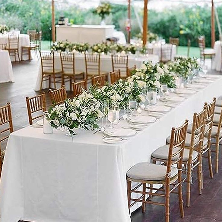 a long table is set up with white linens and green floral centerpieces