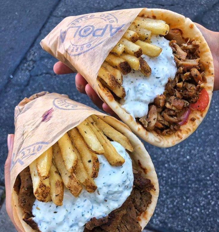 two sandwiches with french fries and sauce on them are being held by someone's hand