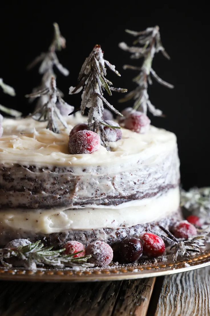 there is a cake with frosting and berries on the top, sitting on a wooden table