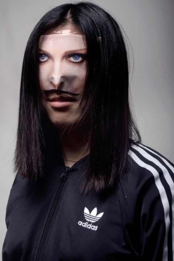 a woman with fake moustache on her face wearing a adidas track jacket