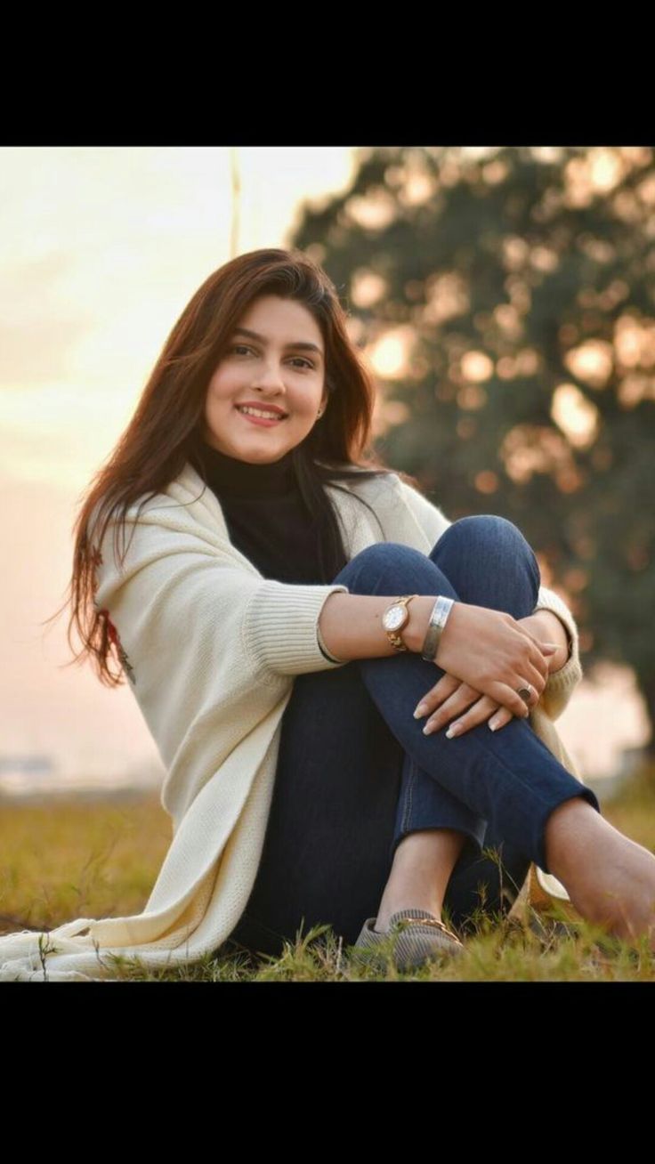 a woman sitting in the grass with her arm around her chest and smiling at the camera