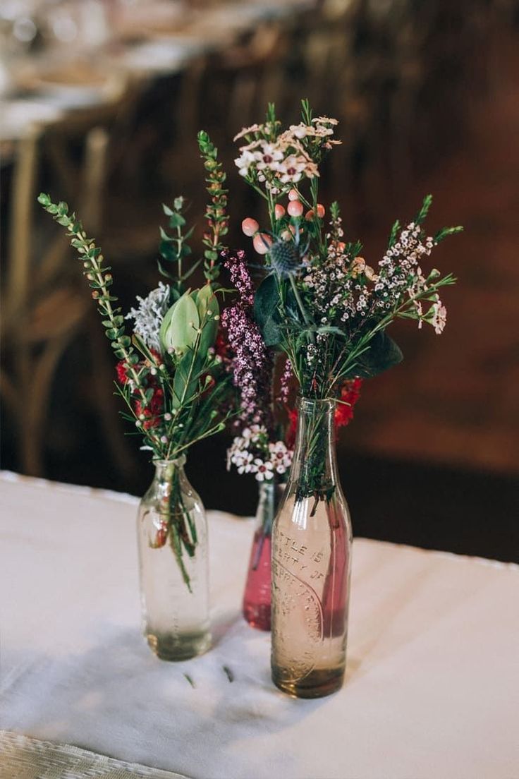 two vases filled with flowers sitting on top of a white tablecloth covered table