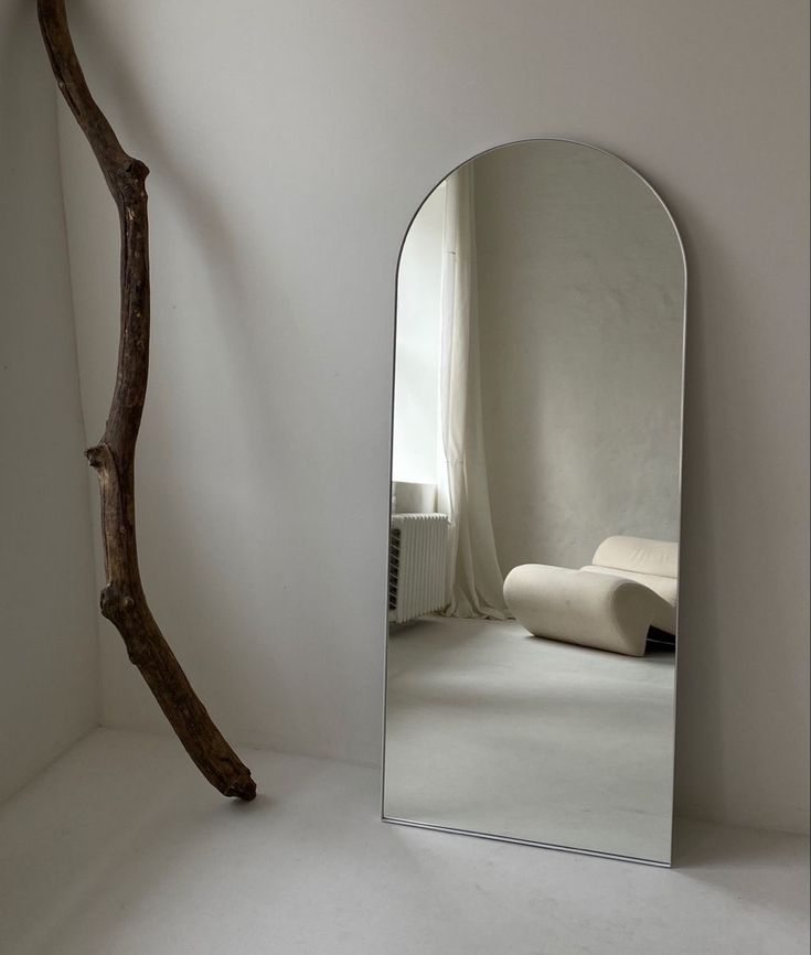 a mirror sitting on top of a white floor next to a tree branch in a room