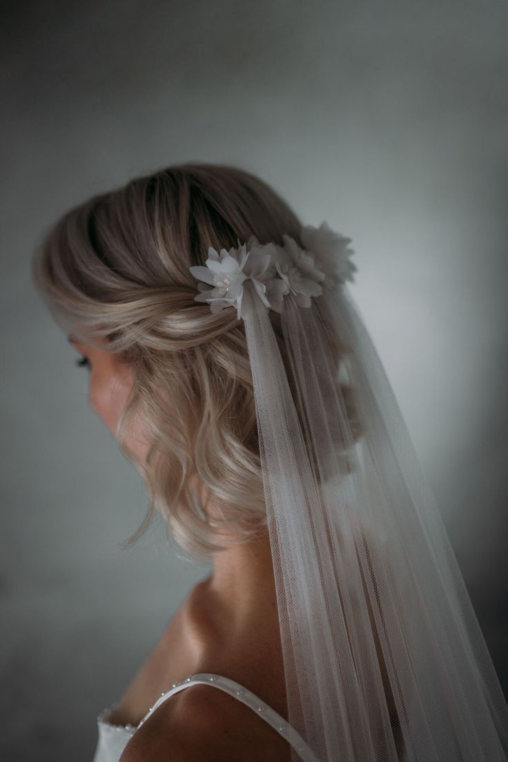 a woman wearing a veil with flowers on it's head and her hair pulled back