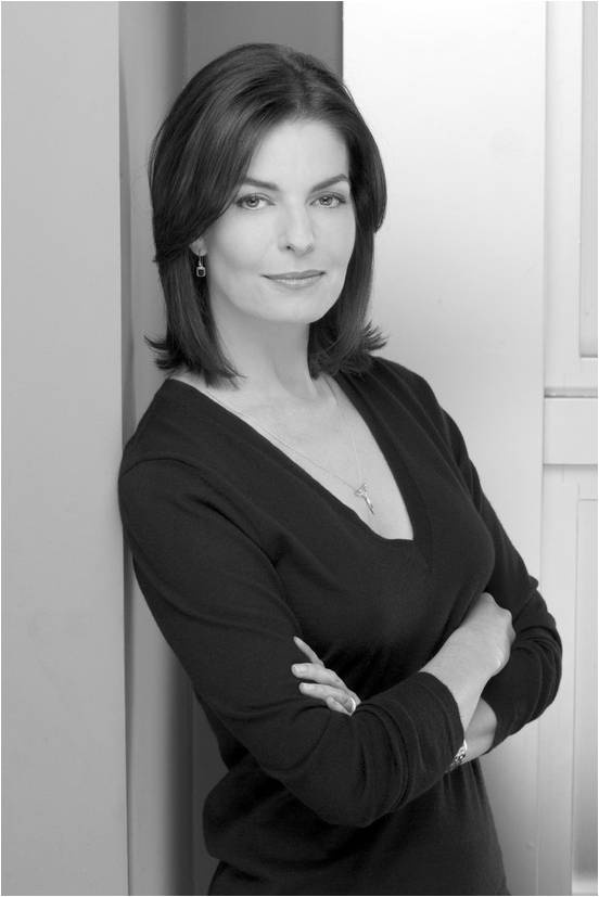 a woman leaning against a wall with her arms crossed and looking at the camera while wearing a black top