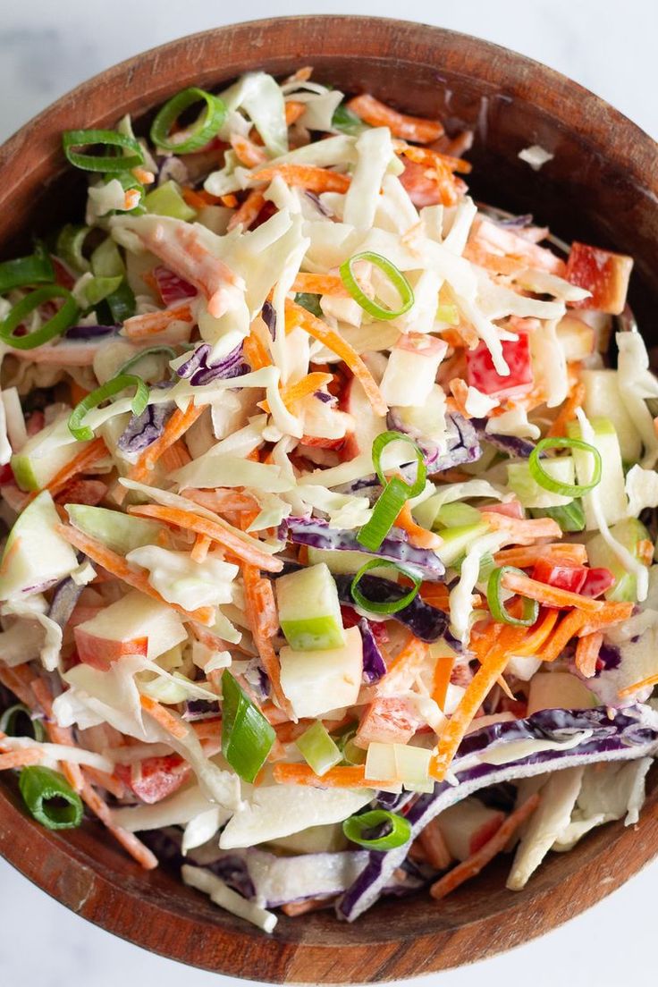 a wooden bowl filled with coleslaw slaw and carrots on top of a white table