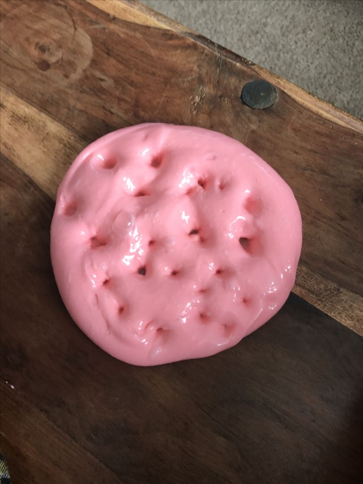 a pink doughnut sitting on top of a wooden cutting board