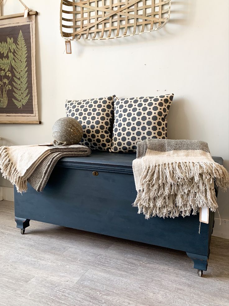 a blue bench with two pillows on it in front of a wall hanging above the bench