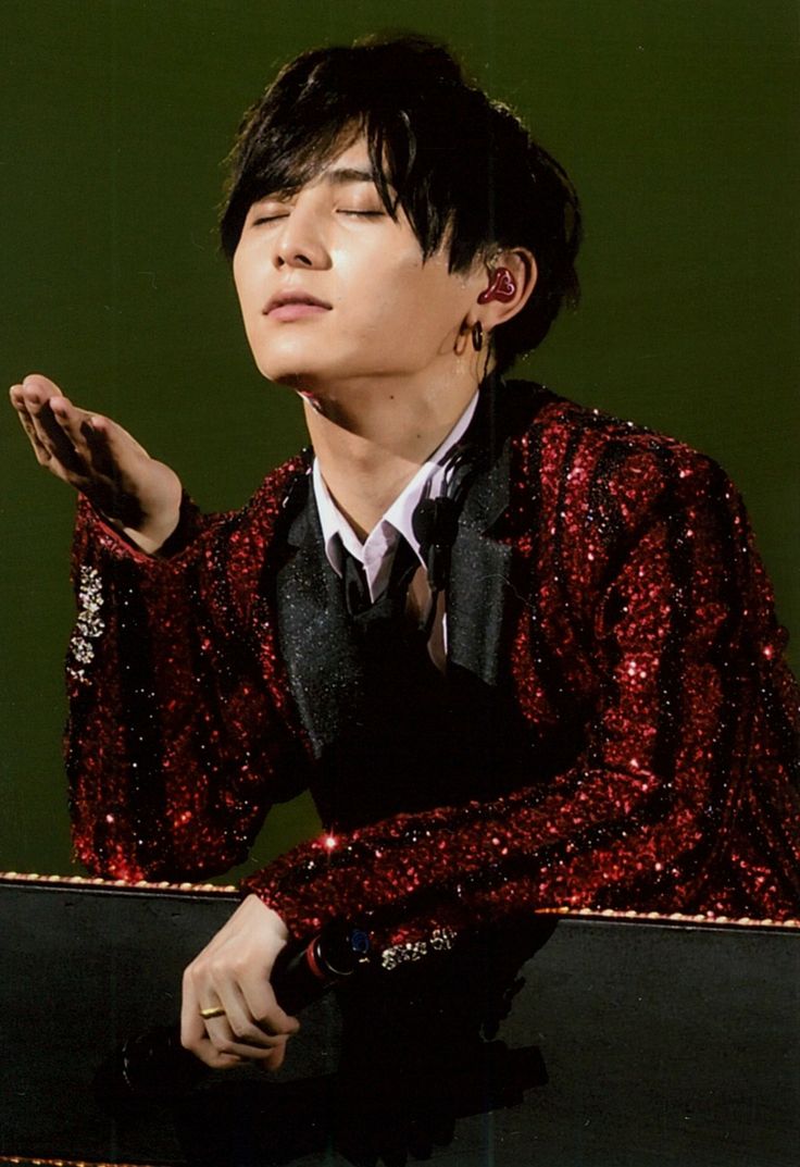 a young man in a red sequin jacket and tie sitting on a skateboard