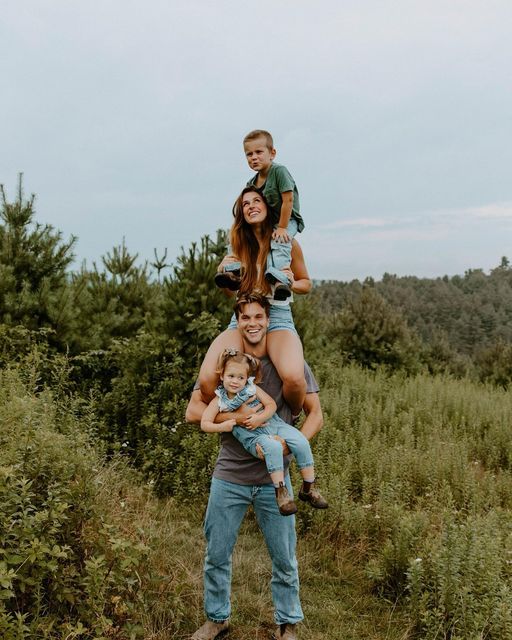 a man is holding two children while standing on his shoulders in the middle of a field