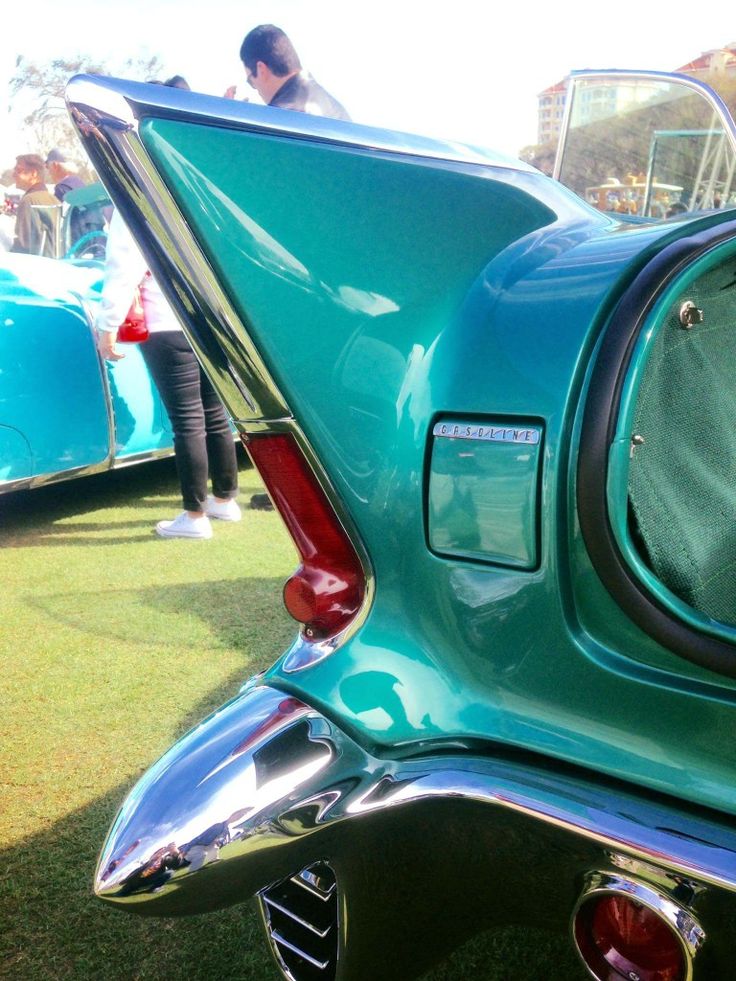 the rear end of an old car with its door open and people in the background