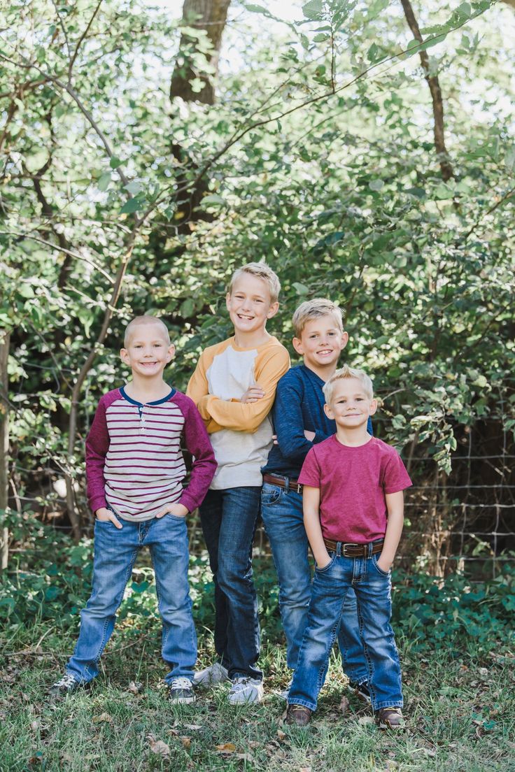 a group of young boys standing next to each other in front of trees and bushes