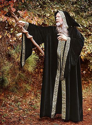 an old man dressed in black and holding a stick with his right hand while standing next to a tree