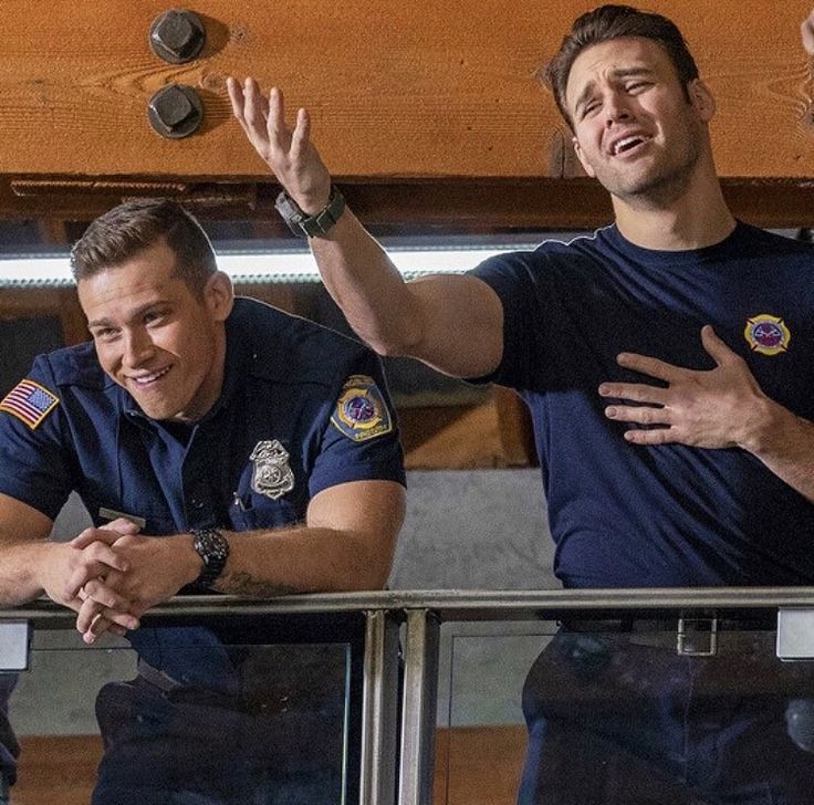 two men in police uniforms standing next to each other on a balcony with their hands up