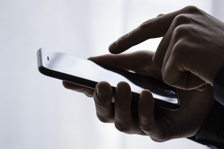 a person holding a smart phone in their hand and touching the screen with both hands