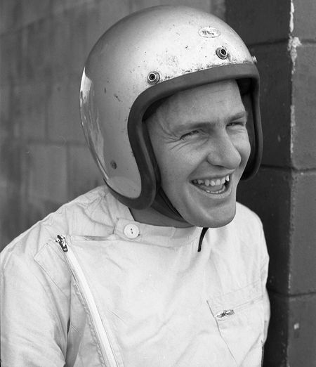 a man wearing a helmet and smiling in front of a brick wall with his hand on his hip