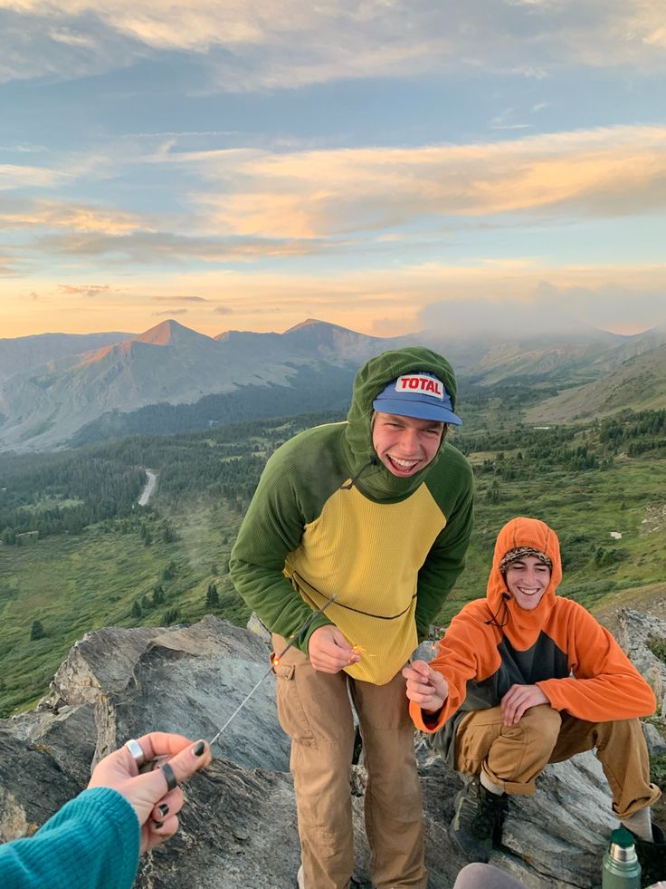 two people standing on top of a mountain with mountains in the background and one person holding a cell phone