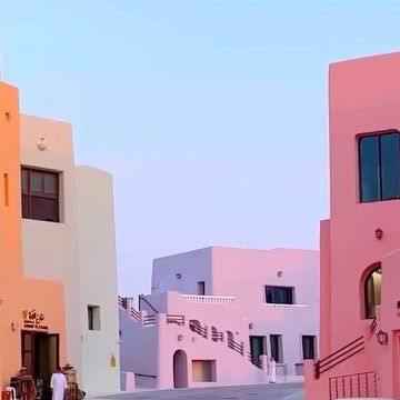 some people are walking down the street in front of pink buildings