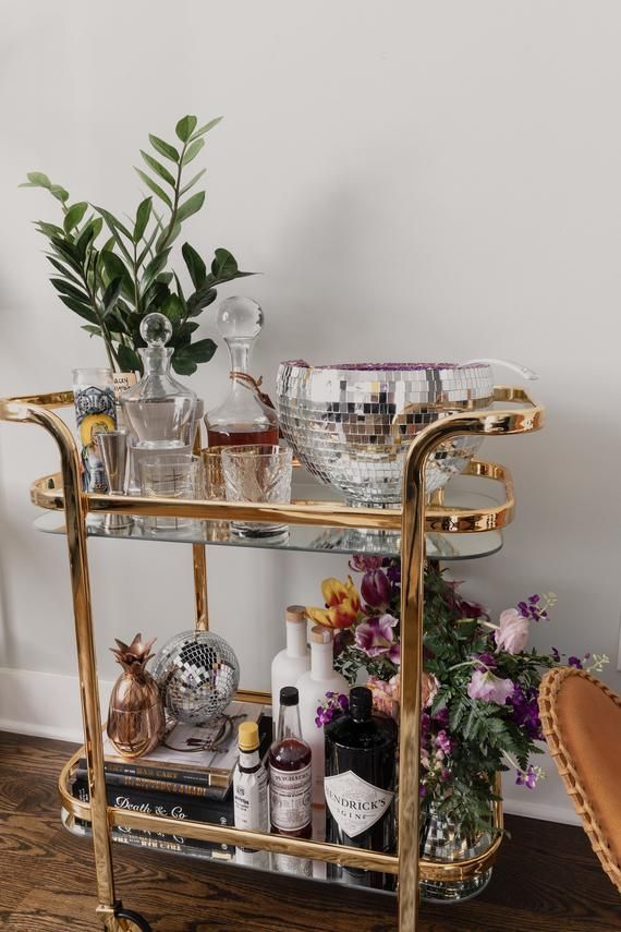 a gold bar cart filled with bottles and glasses on top of a hard wood floor