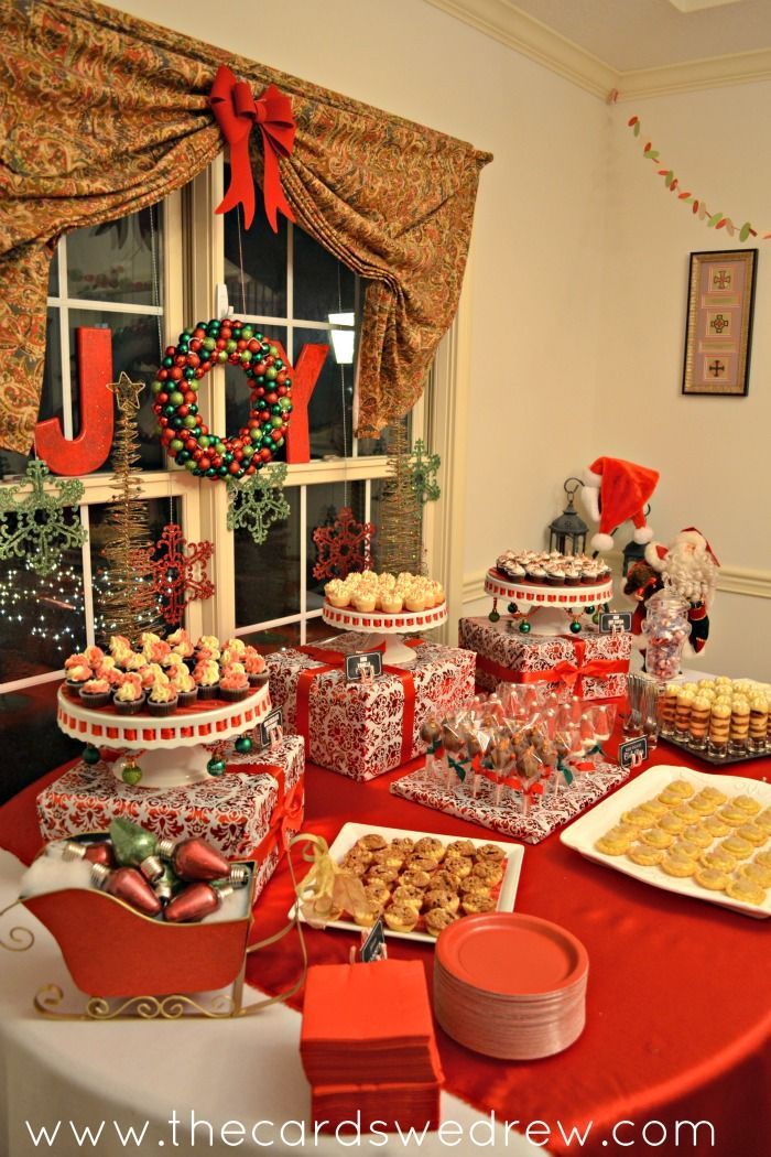 a red table topped with lots of desserts next to a christmas tree filled window