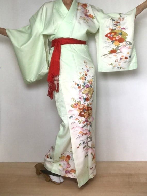 "An embroidered Kimono dress in pale green.  Japanese fans, Maple leaf and chrysanthemum floral pattern floating in pink clouds.  2 bottom front fans with embroidered outline in metallic gold thread. Fits a USA women's size M. International Express Shipping Includedsee below) MATERIAL:  Synthetic with synthetic lining.   PATTERN:  Chrysanthemums, Maple leaf, clouds and embroidered fans. COLOR:  Pale green, pink, oranges, teal, gold mustard, avocado green & metallic gold. CONDITION:  Used, vintage.  A few very faint, tiny stains / seamstress dots along some seams (see photos).  Clean interior.  Sash NOT included. Kimono sash sold separately. Kimono are DRY CLEAN only. My shop: https://kimonomemoirs.etsy.com. SIZE: Women's size MEDIUM Kimono. (Model is 5'7\" wearing 1.5\" platform sandal) Wi Kimonos, Kawaii, Japanese Kimono Dress, Green Sash, Lining Pattern, Yellow Kimono, Japanese Fans, Floral Dress Vintage, M Video