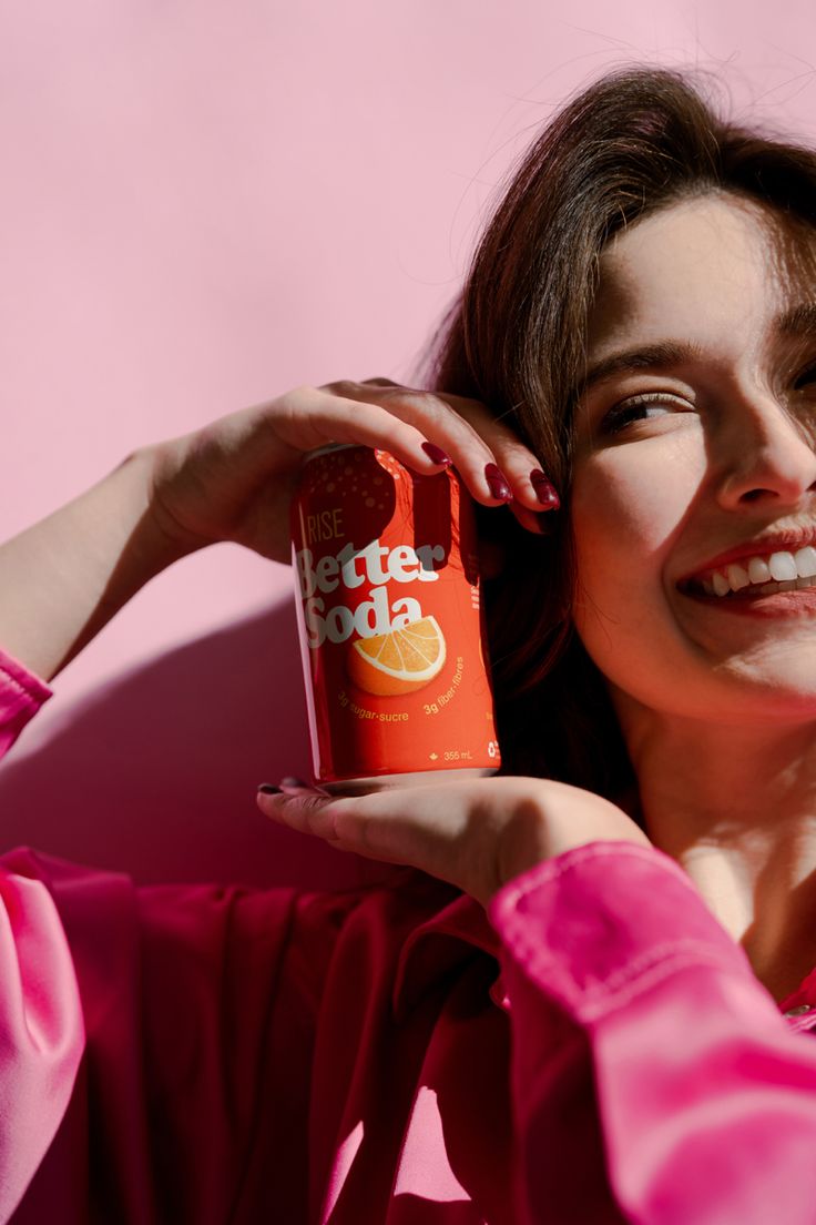 a woman in pink shirt holding up a can of orange juice to her face and smiling