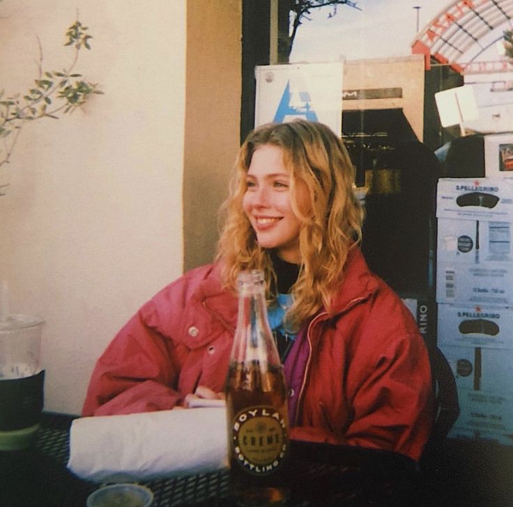 a woman sitting at a table with a bottle of beer