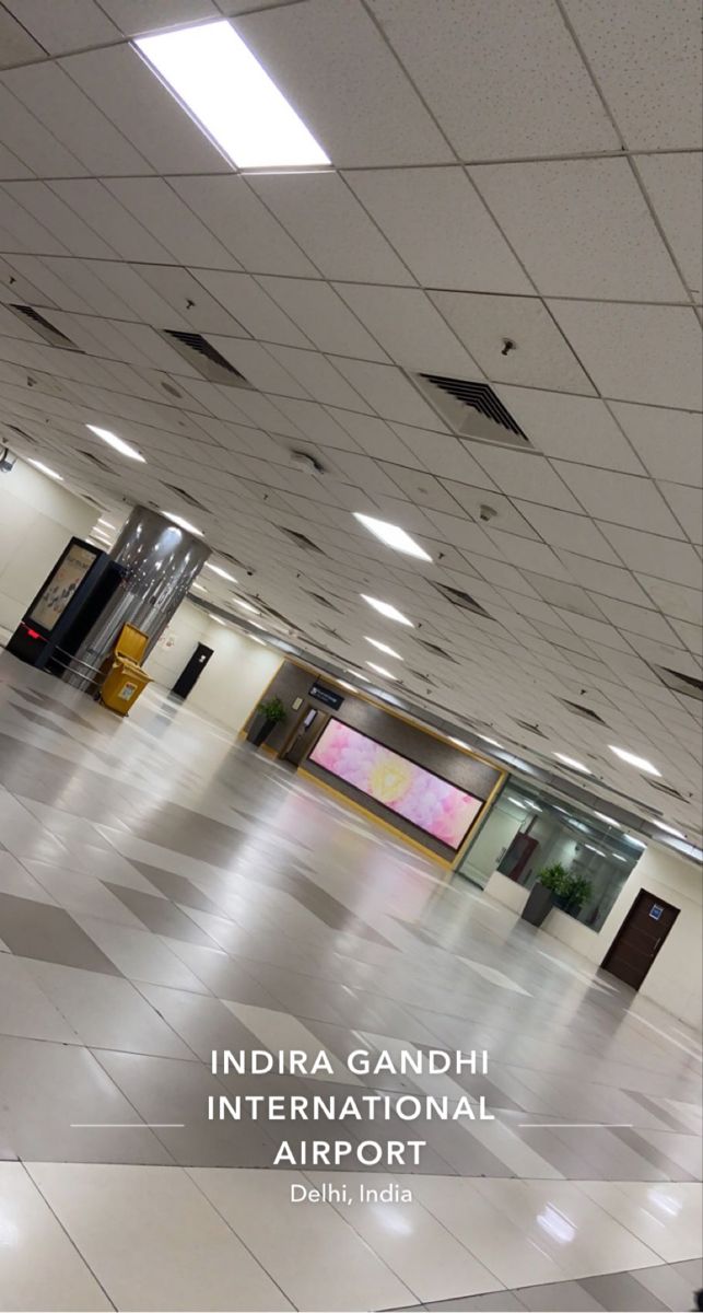 the inside of an airport with white tile floors and ceiling tiles on both sides, there is a sign that says india gandhi international airport